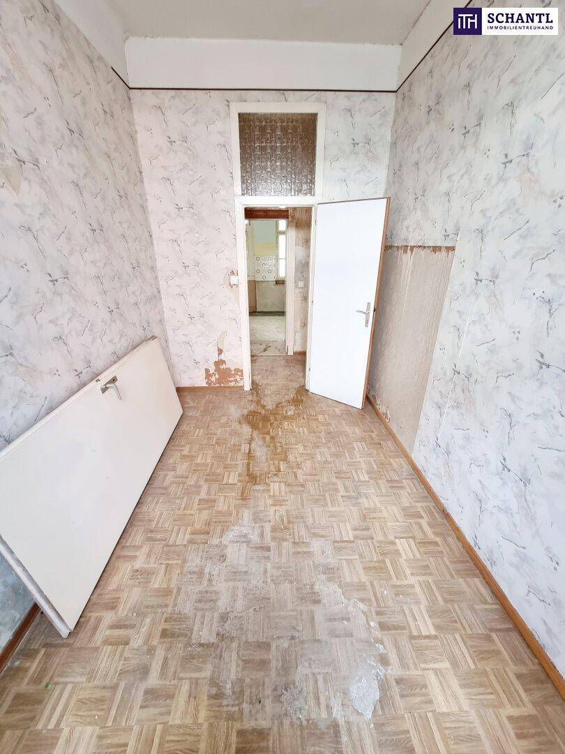 Leeres Zimmer mit abgenutztem Parkettboden und alter Tapete, das auf eine umfassende Renovierung wartet.