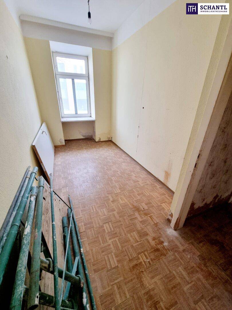 Leeres Zimmer mit Fischgrätparkett und einem Fenster, das auf die Straße blickt, im Renovierungszustand.