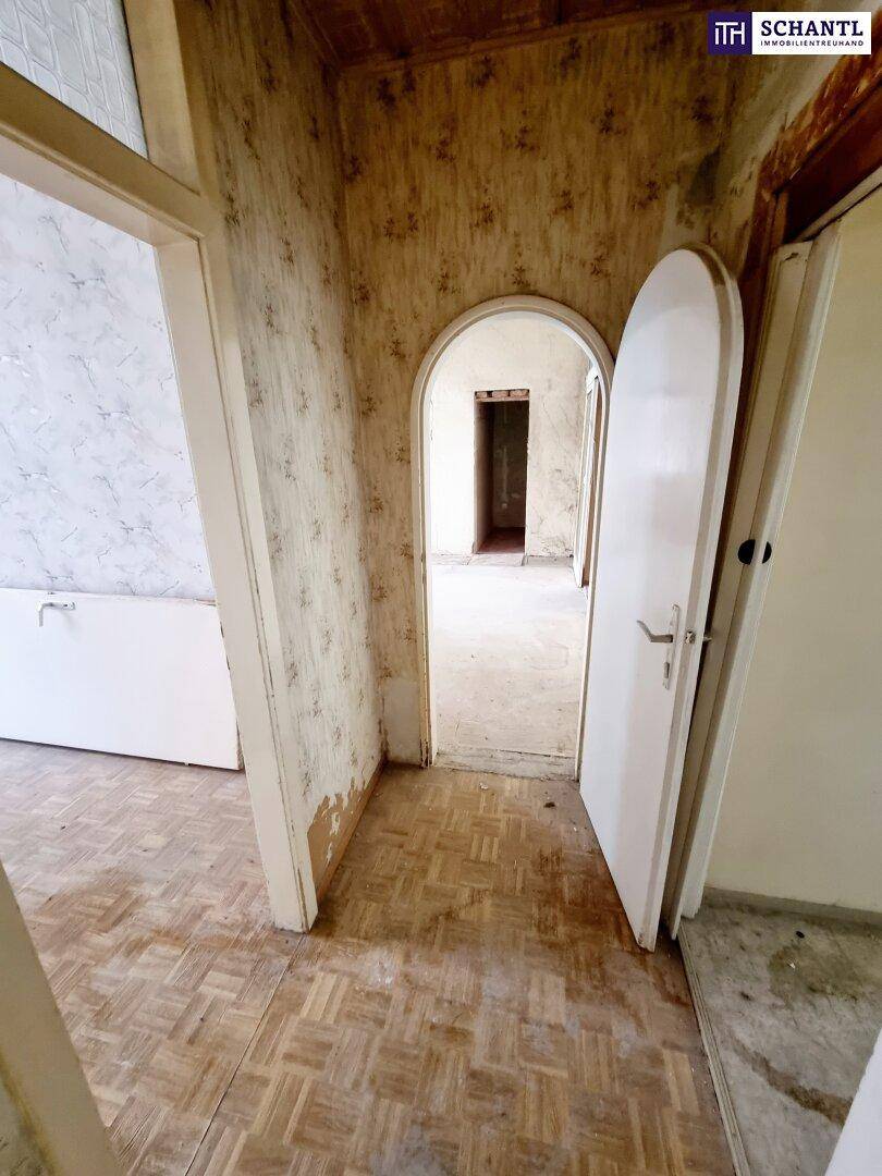 Flur mit einem charakteristischen Rundbogen und abgenutztem Parkettboden, der renoviert werden muss.