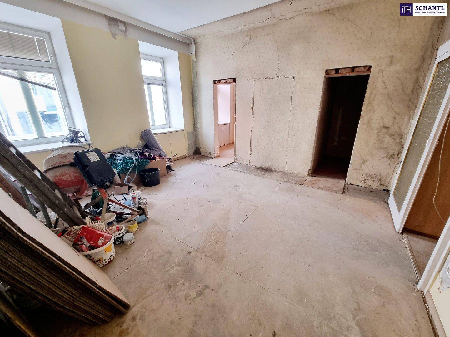 Geräumiger Innenraum im Rohzustand mit Baugeräten und abgenutzten Wänden, bereit für die Renovierung.