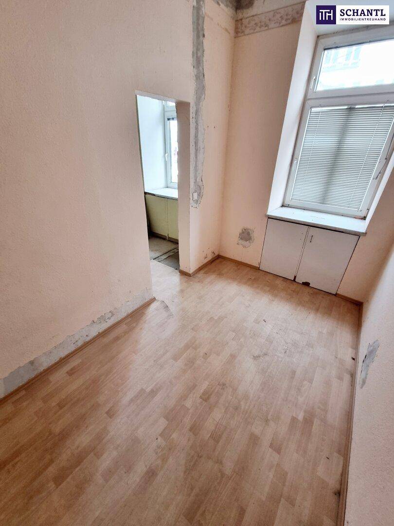 Leeres Zimmer mit hellem Holzboden und einem Fenster mit Jalousien, das auf eine Renovierung wartet.