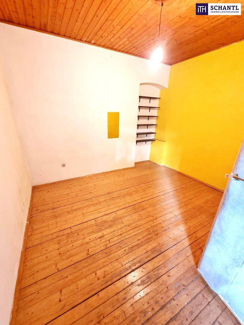 Helles Zimmer mit Holzdielenboden, gelber Wand und Holzdecke.