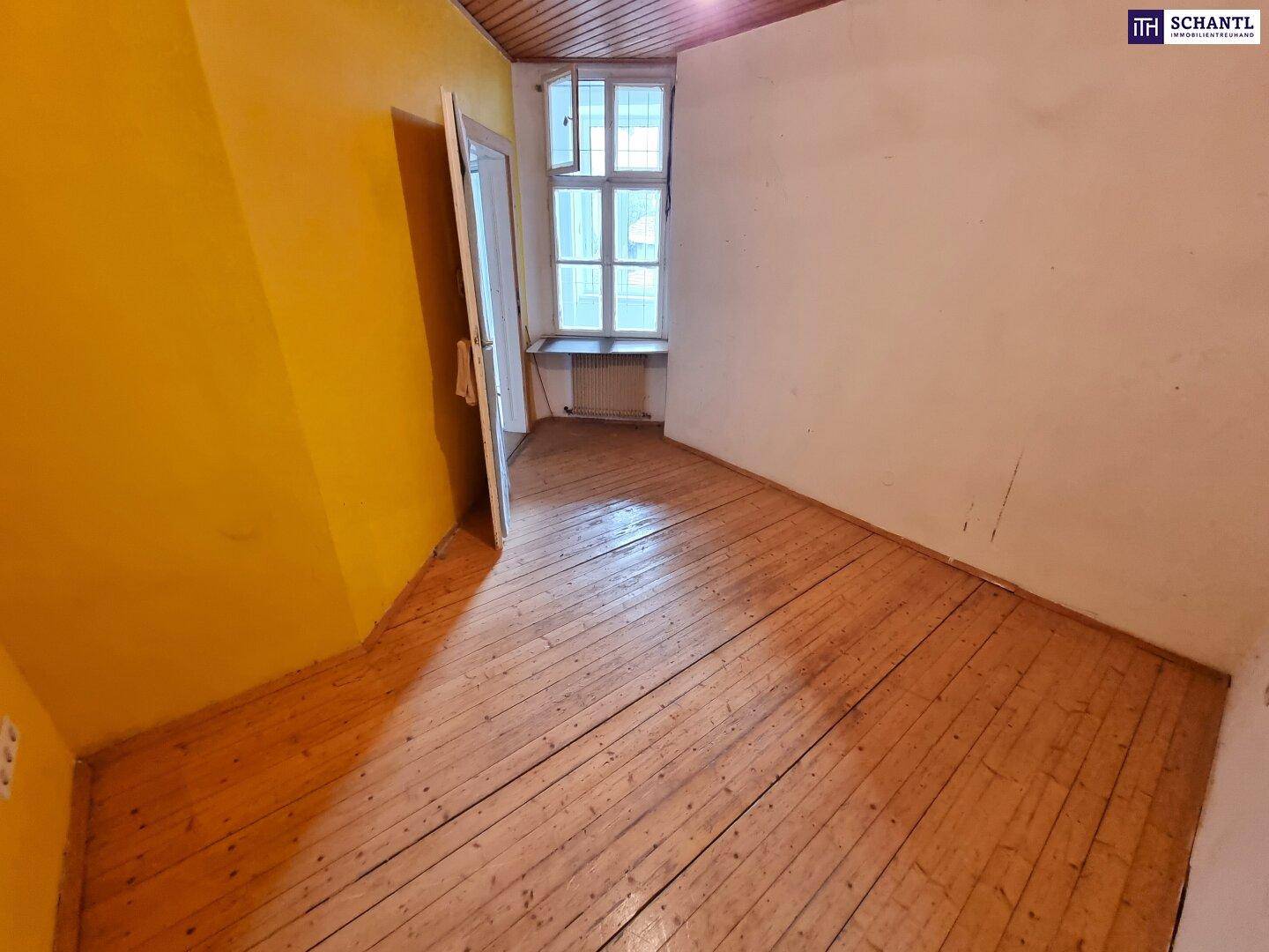 Zimmer mit Holzdielenboden, gelber Wand, Fenster und Holzdecke.