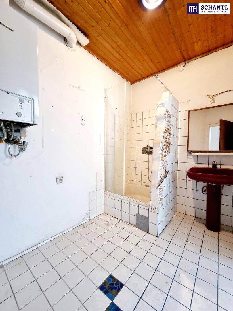Badezimmer mit Duschkabine, Fliesenboden und Holzdecke, renovierungsbedürftig.
