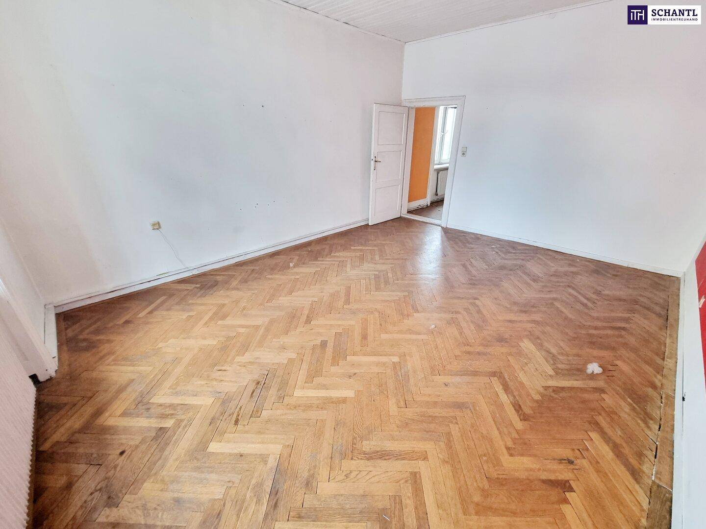 Geräumiges Zimmer mit Fischgrätparkett, weiß gestrichenen Wänden und viel Tageslicht.