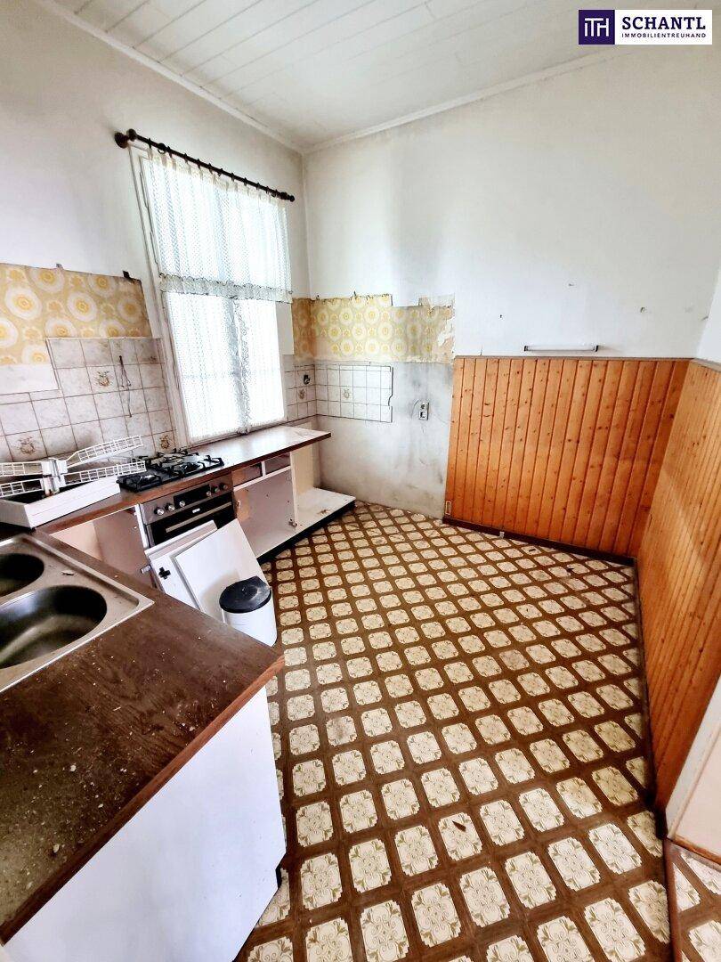 Alte Küche in Renovierungszustand mit Spüle, Herd und Holzverkleidung, bereit zur Modernisierung.