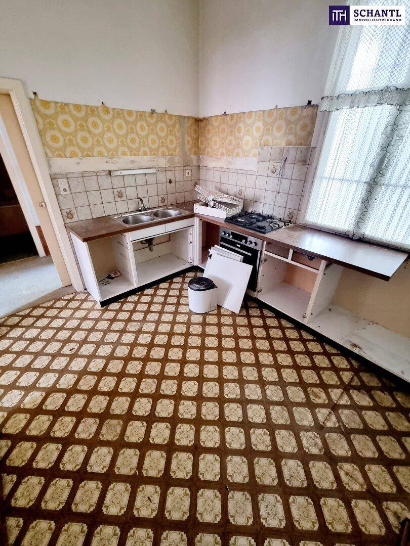 Blick in eine renovierungsbedürftige Küche mit Spüle, Herd und teilweise entfernter Einrichtung.