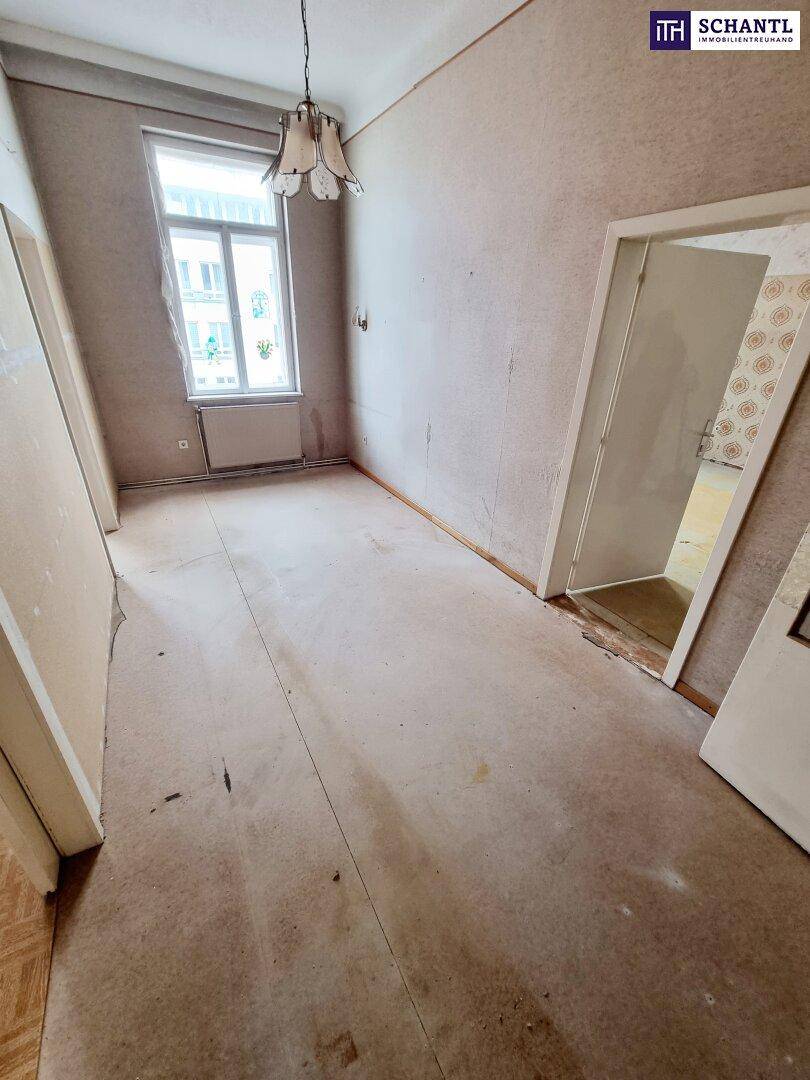Renovierungsbedürftiger Raum mit alter Tapete, Teppichboden und Fenster, bereit zur Neugestaltung.