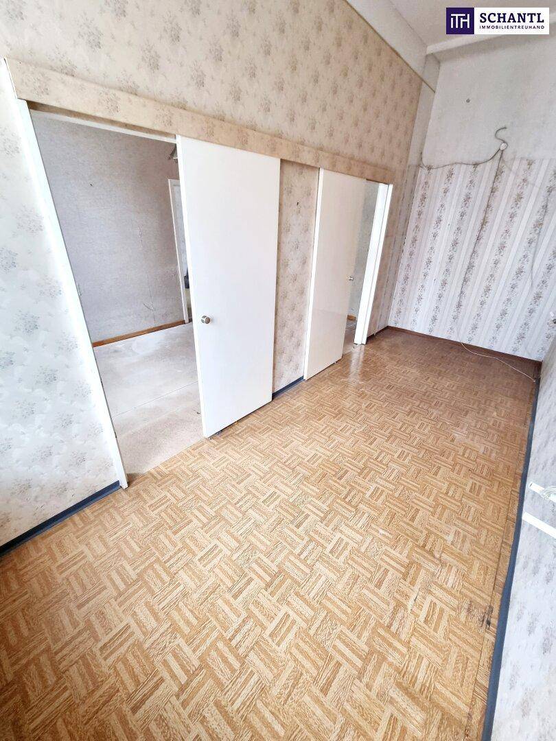 Schmaler Flur mit gemusterter Tapete und altem Parkettboden, der zu weiteren Räumen führt.