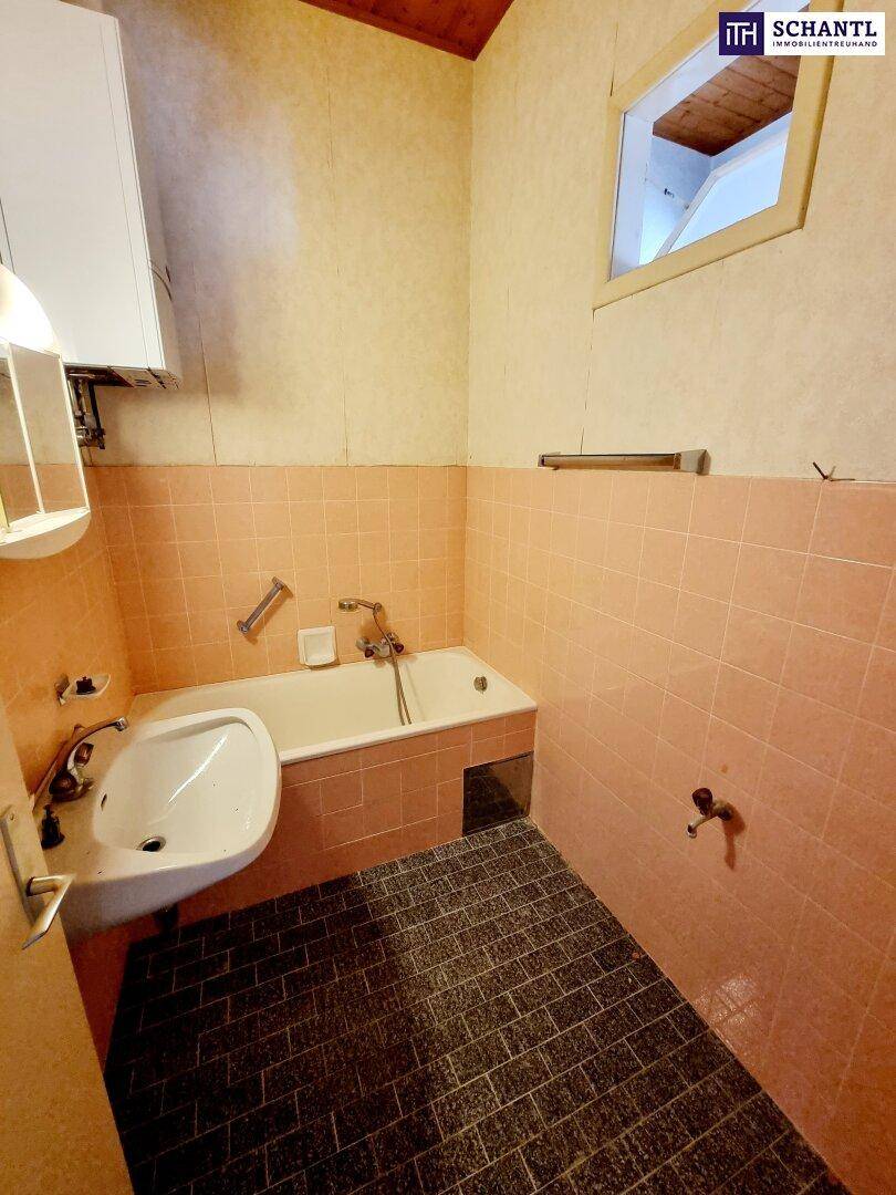 Kleines Badezimmer in Renovierungszustand mit Badewanne, Waschbecken und Fenster.
