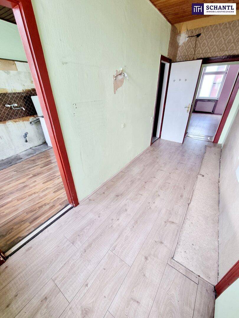 Flur mit Laminatboden und Blick in einen Küchenbereich, der renoviert werden muss.