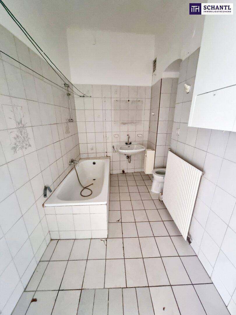 Badezimmer mit weißen Fliesen, Badewanne und WC, das eine Modernisierung benötigt.