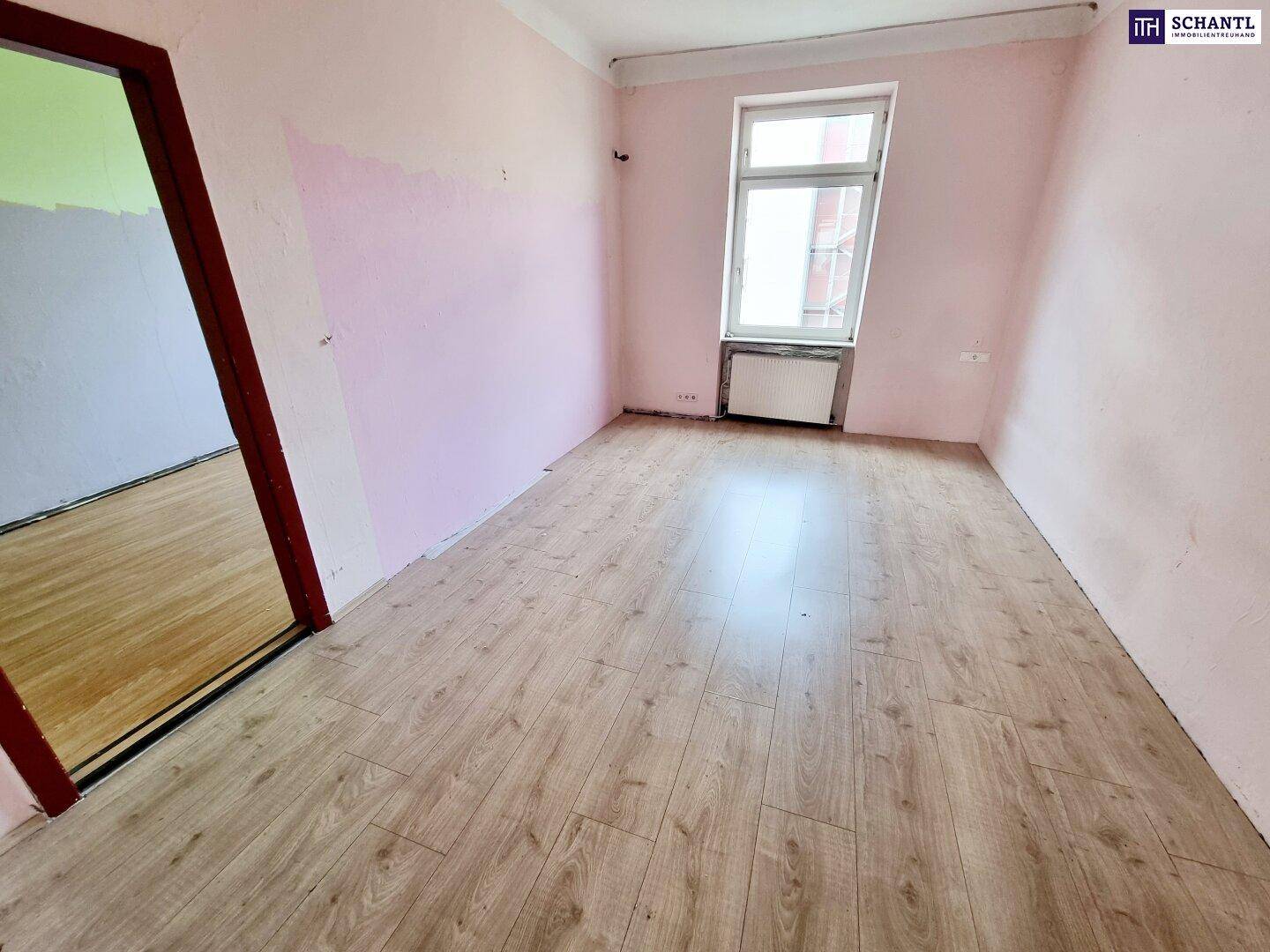 Geräumiger Raum mit Laminatboden und rosa gestrichenen Wänden, bereit für Renovierung.