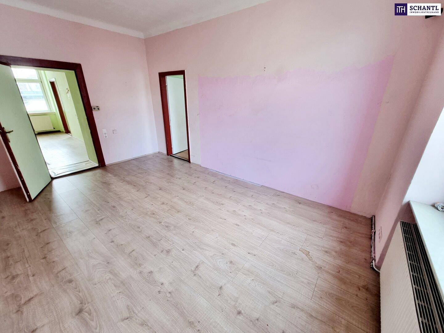 Heller Wohnraum mit Laminatboden und rosa Wänden, der auf eine Neugestaltung wartet.