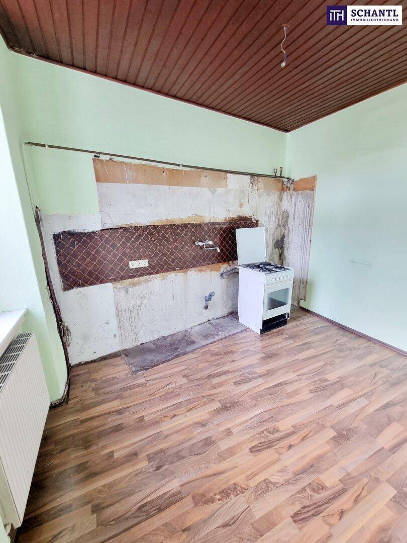 Leere Küche mit Laminatboden und Gasherd, die eine umfassende Modernisierung benötigt.
