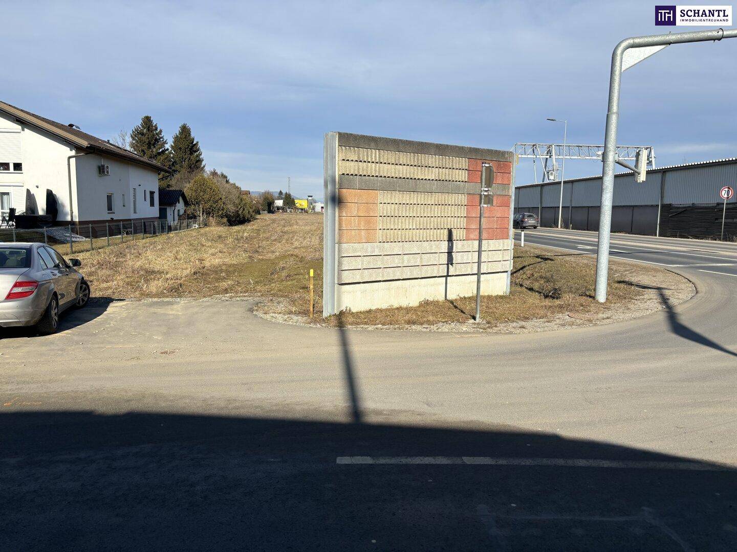 Straßenecke mit einem Abschnitt der Lärmschutzwand und einem geparkten Auto vor Wohnhäusern.