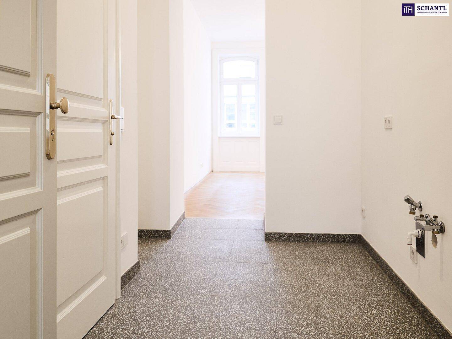 Langer Flur mit Terrazzoboden und sichtbaren Wasseranschlüssen, führt zu weiteren Räumen.