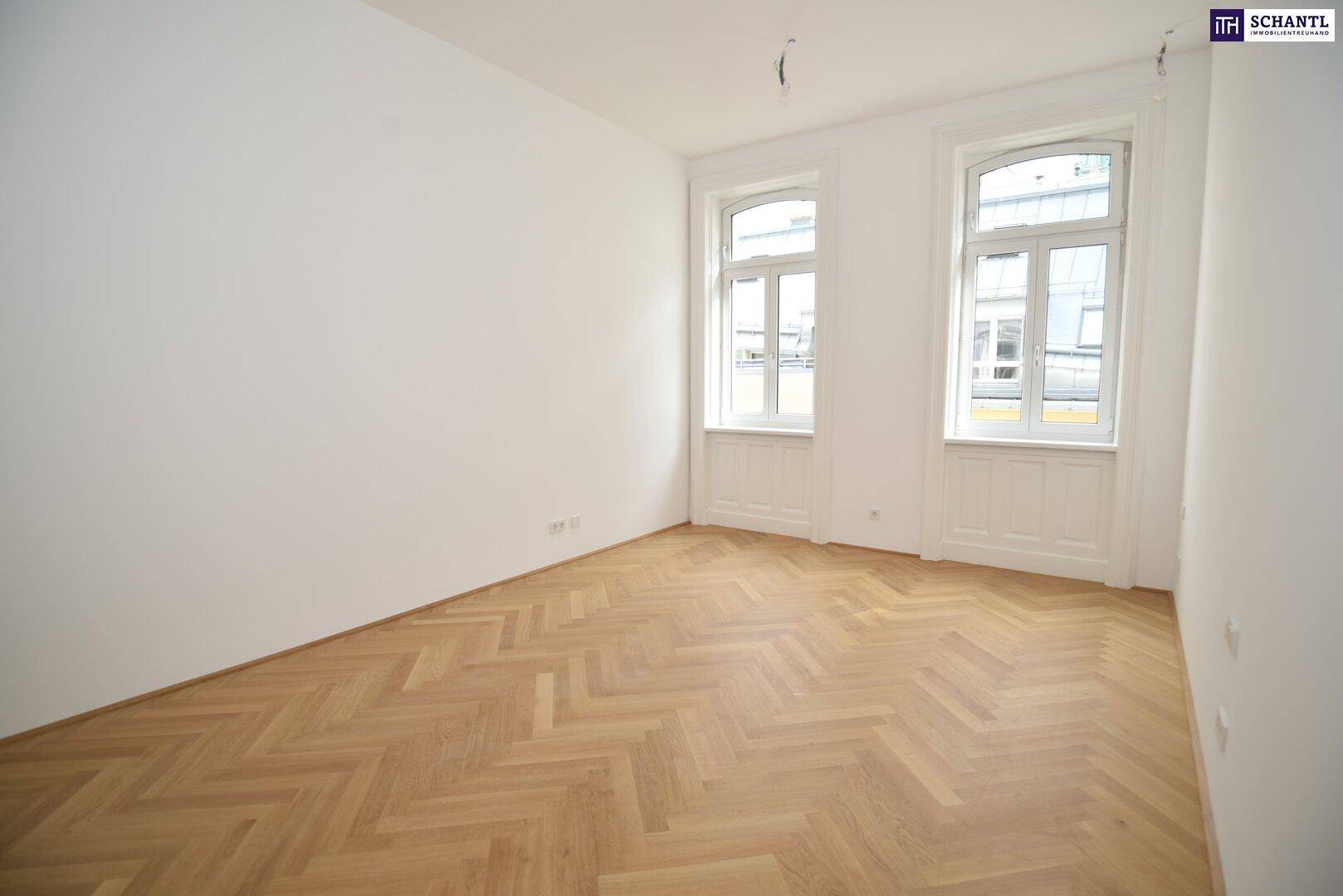 Lichtdurchfluteter Raum mit zwei hohen Fenstern und elegantem Fischgrätparkettboden.