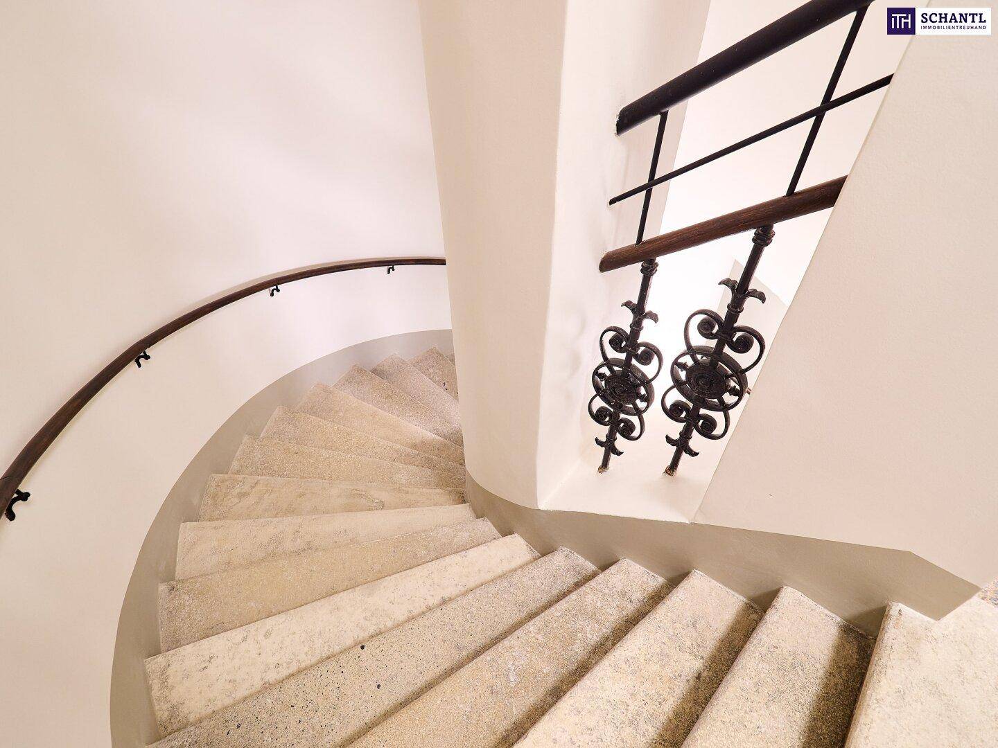 Geschwungene Steintreppe mit schlichtem Handlauf in einem hellen Treppenhaus.
