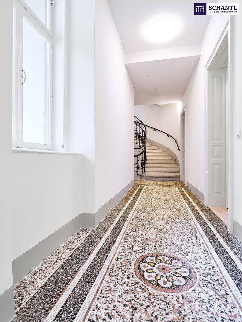 Langer Flur mit kunstvollem Mosaikboden, hohen Fenstern und Zugang zum Treppenhaus.