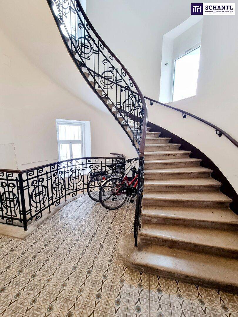 Geschwungene Steintreppe mit kunstvollem schmiedeeisernem Geländer und gemusterten Fliesen im Treppenhaus.
