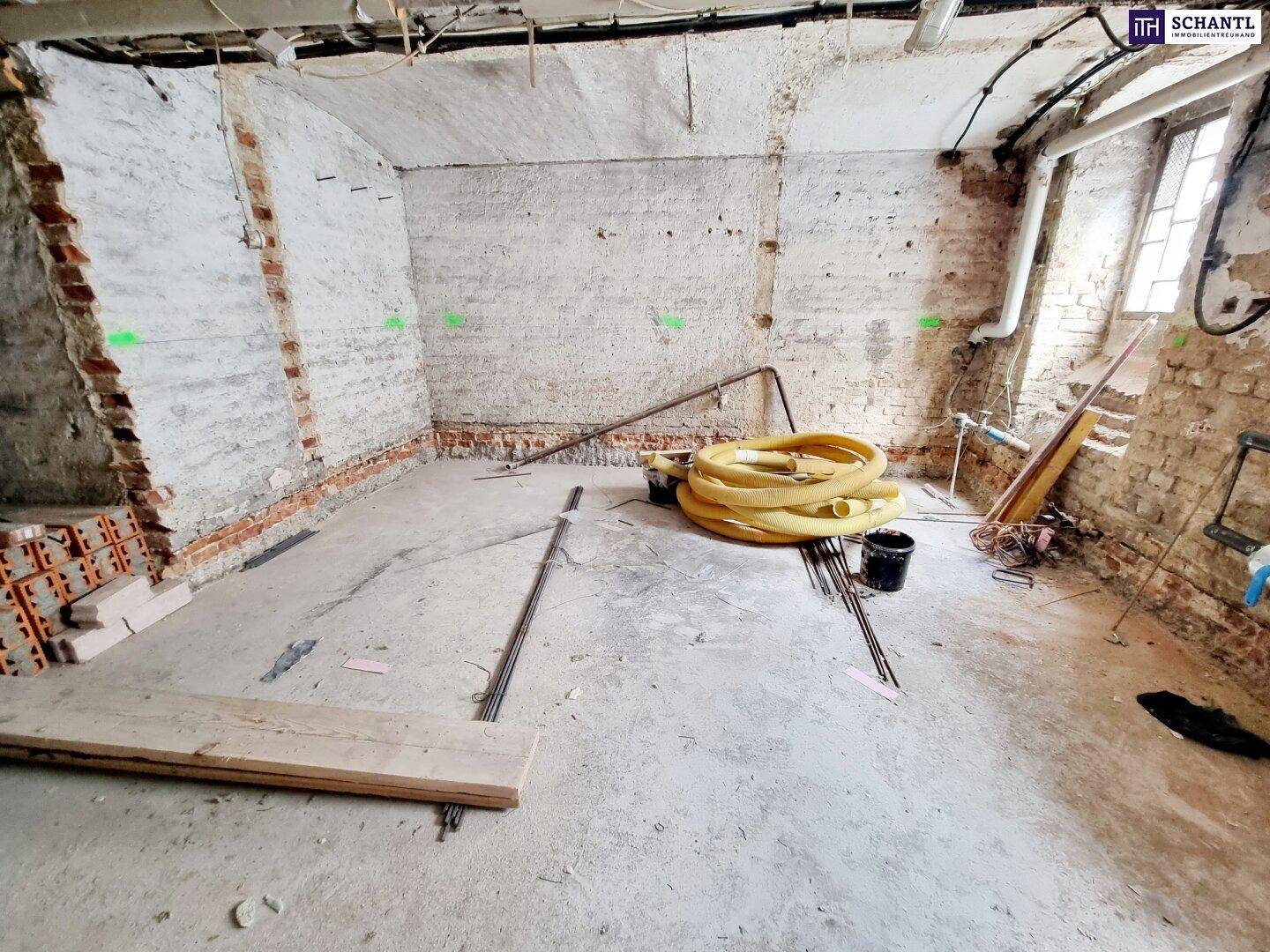 Großer Rohbau-Raum mit sichtbaren Ziegelwänden und Baumaterialien auf dem Boden.