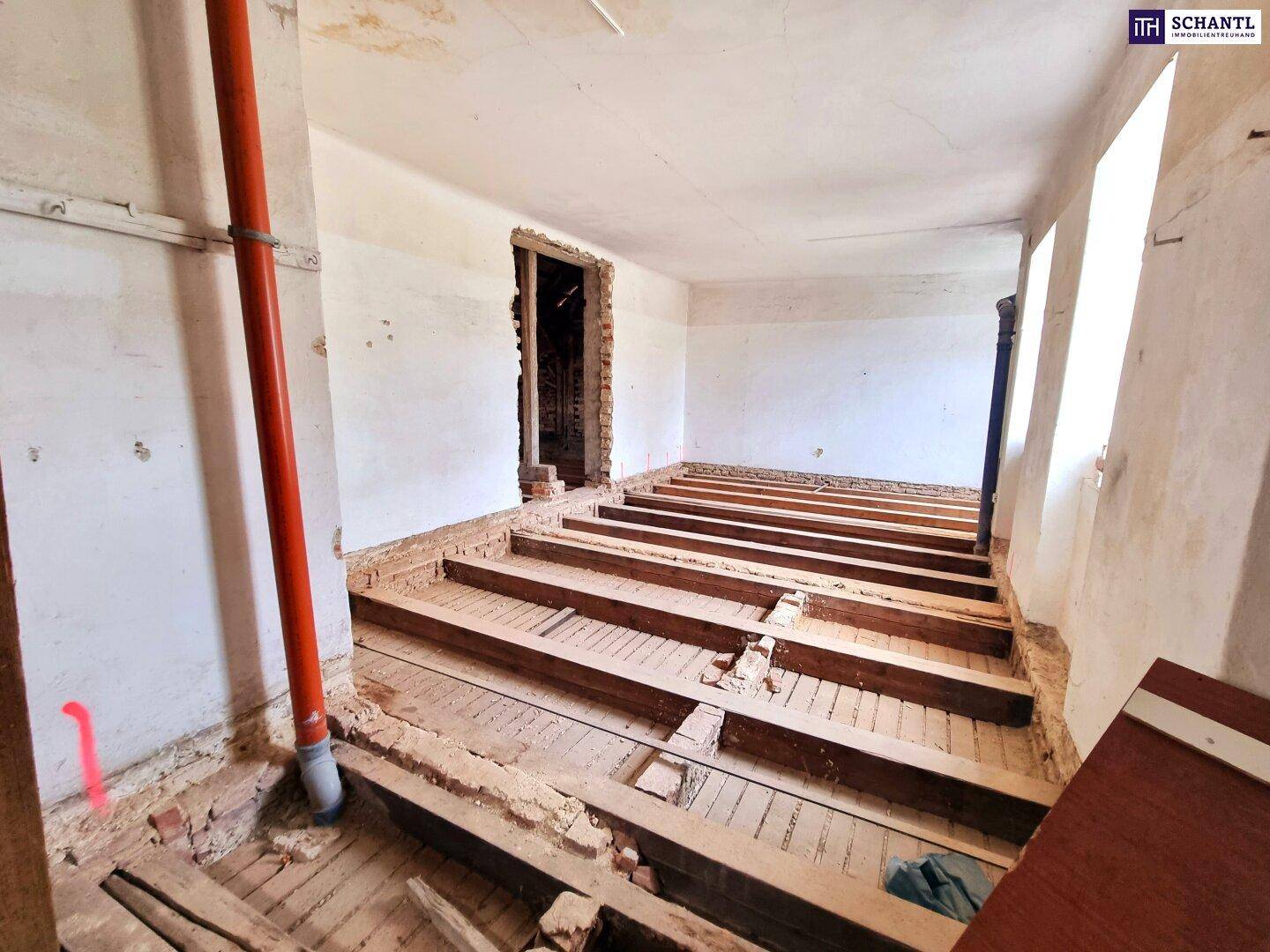 Rohbauzimmer mit freigelegten Holzbalken und einer roten Leitung an der Wand.