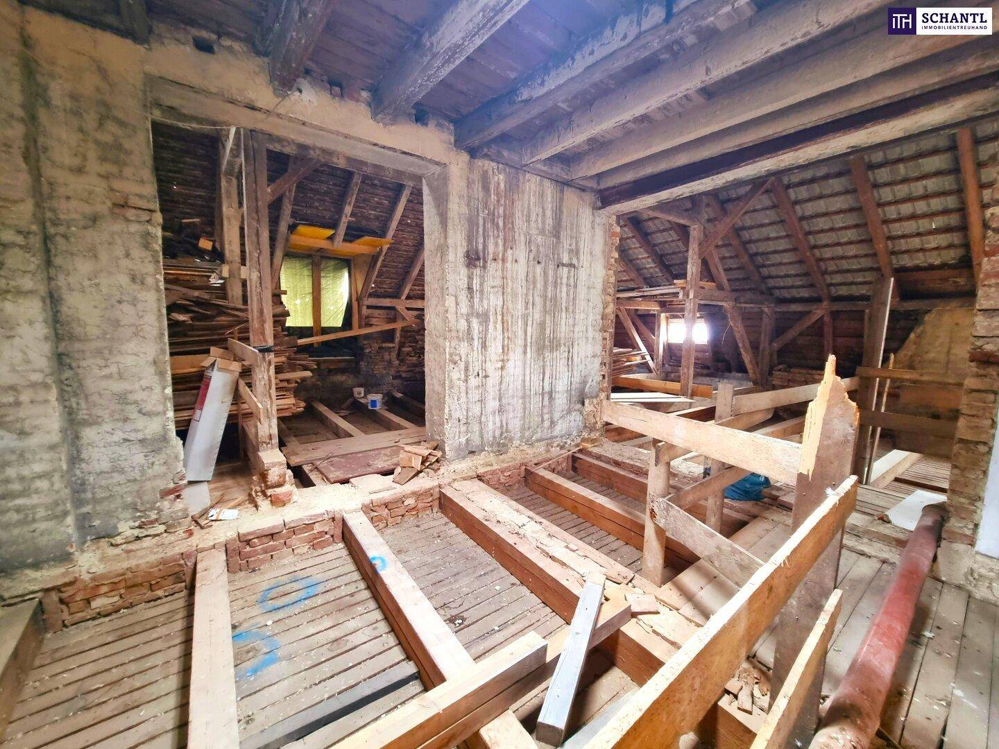 Rohbauzimmer mit Blick in den Dachbodenbereich, gekennzeichnet durch freiliegende Holzkonstruktionen.