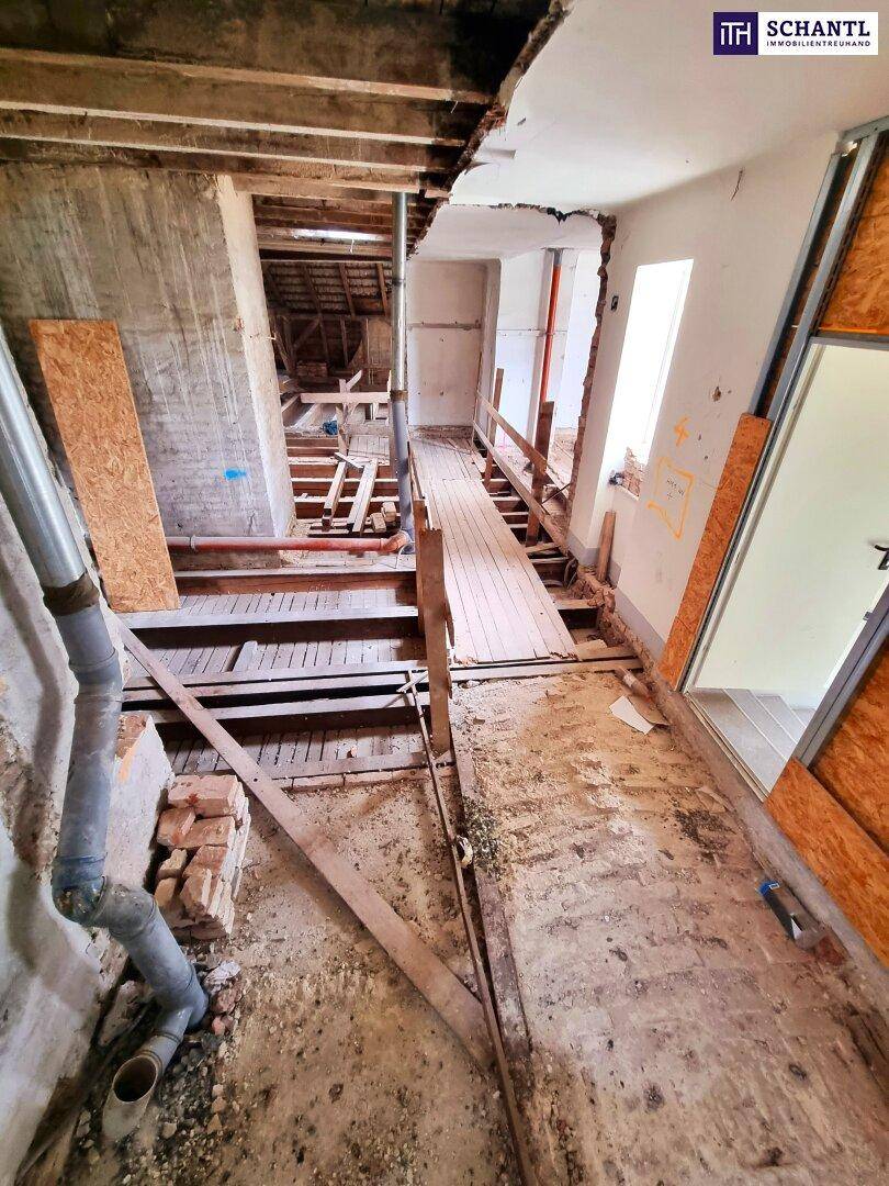 Innenraum im Rohbauzustand mit sichtbaren Holzbalken und vorbereiteten Bodenstrukturen.
