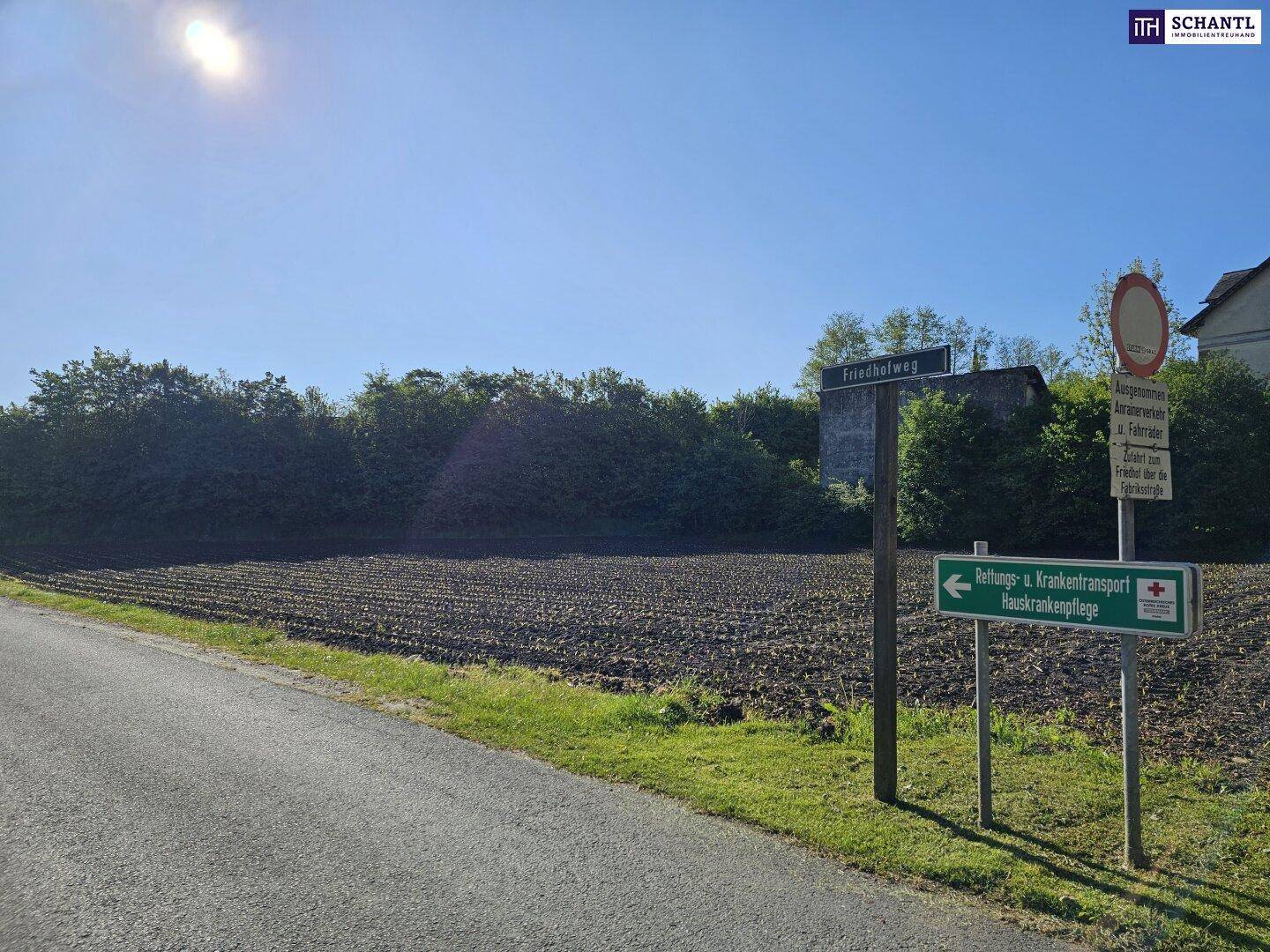 Grundstück mit Hinweisschildern am Straßenrand, umgeben von Ackerland und Bäumen.