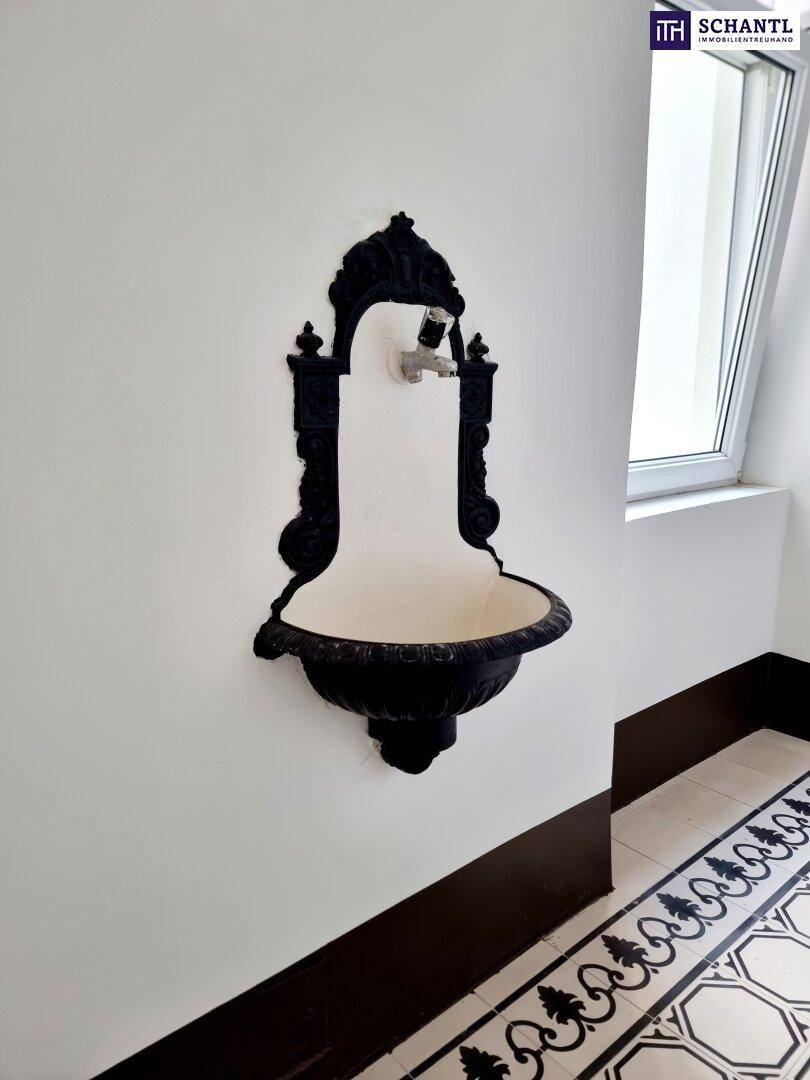 Historischer Flur mit dekorativem Wandbrunnen und gemusterten Fliesen am Boden.