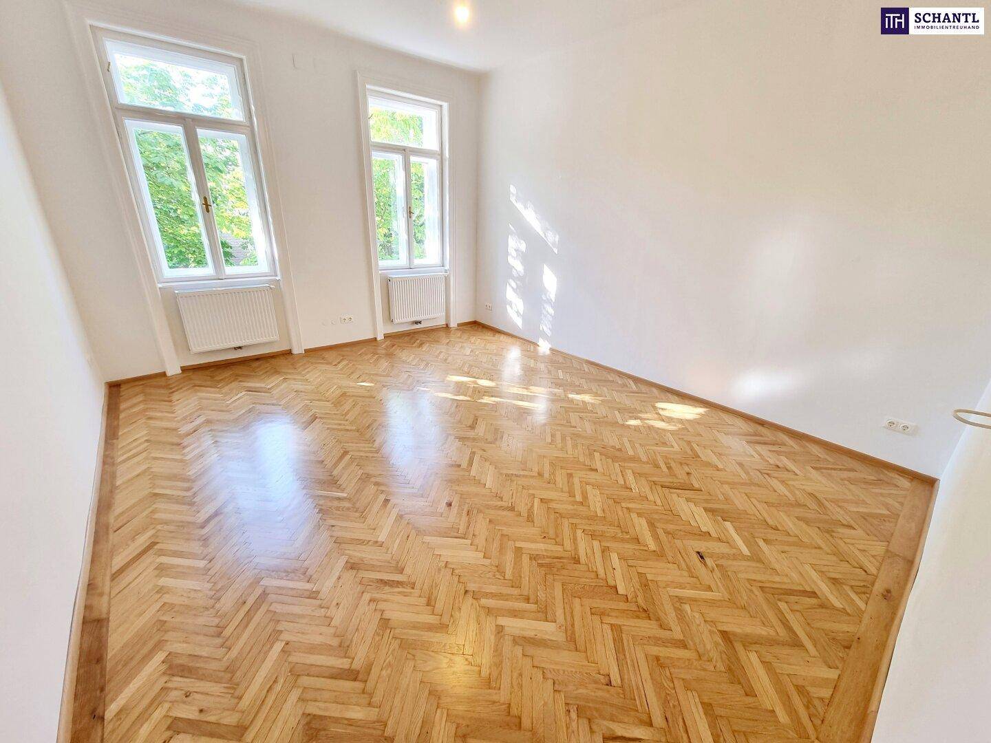 Lichtdurchfluteter Raum mit klassischem Fischgrätparkett und hellen Wänden, ideal für Wohn- oder Schlafzimmer.