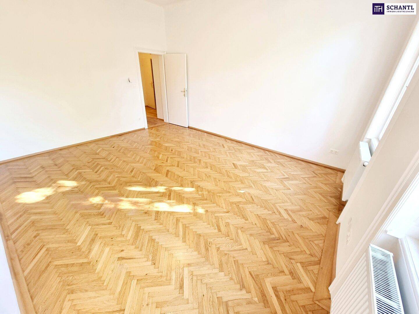 Geräumiges Zimmer mit elegantem Fischgrätparkett, weißen Wänden und Zugang zu weiteren Räumen.