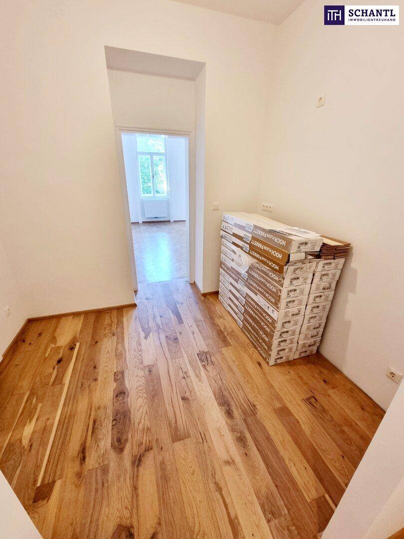 Gangbereich mit neuem Holzplankenboden und gestapelten Materialien, der zu einem weiteren Zimmer führt.