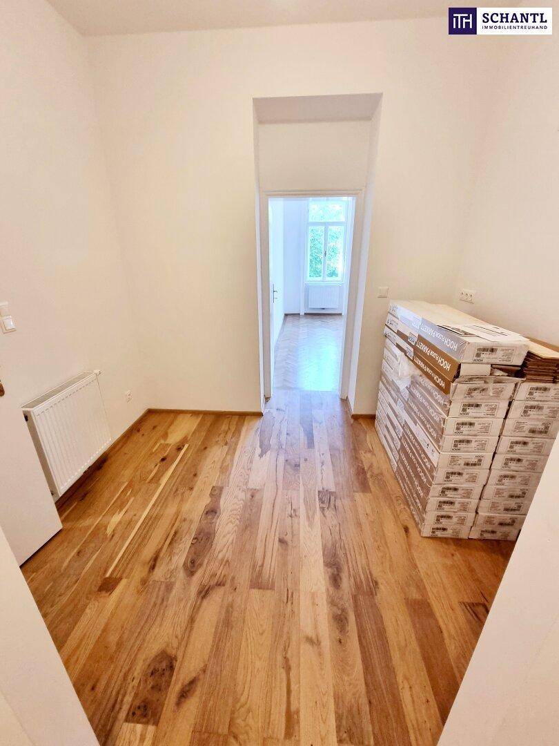 Gangbereich mit Holzplankenboden und gestapelten Materialien, der zu einem hellen Zimmer führt.