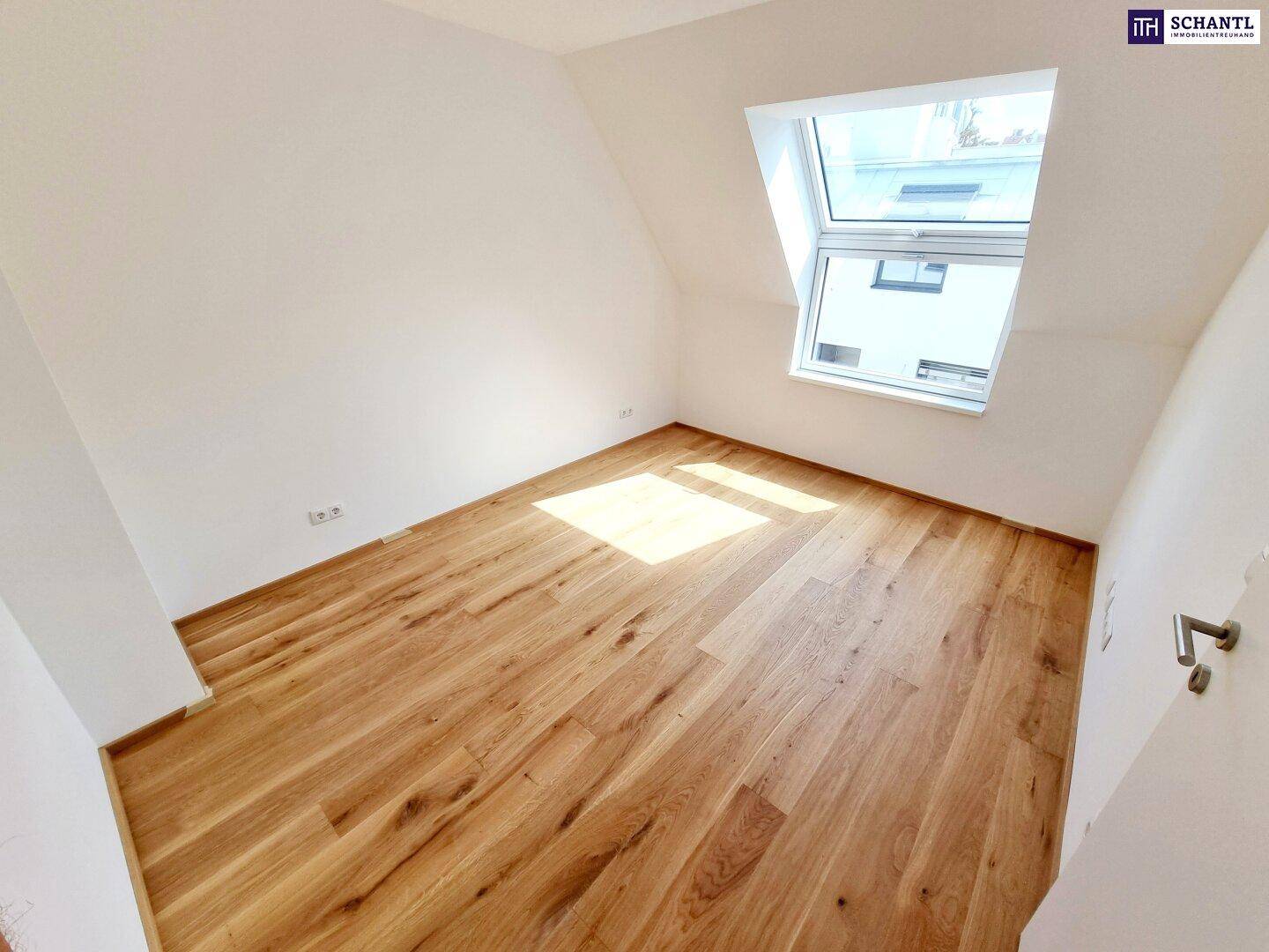 Helles Schlafzimmer im Dachgeschoss mit Holzboden, weißen Wänden und großem Dachfenster.