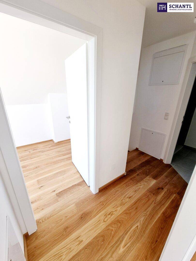 Heller Flur mit Holzboden und weißen Wänden, der zu weiteren Zimmern führt.