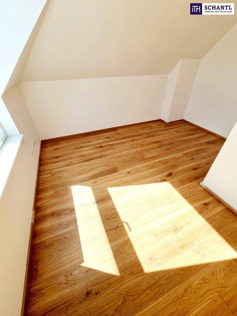 Dachzimmer mit Holzboden und schrägen Wänden, das durch ein Fenster gut belichtet wird und einladend wirkt.
