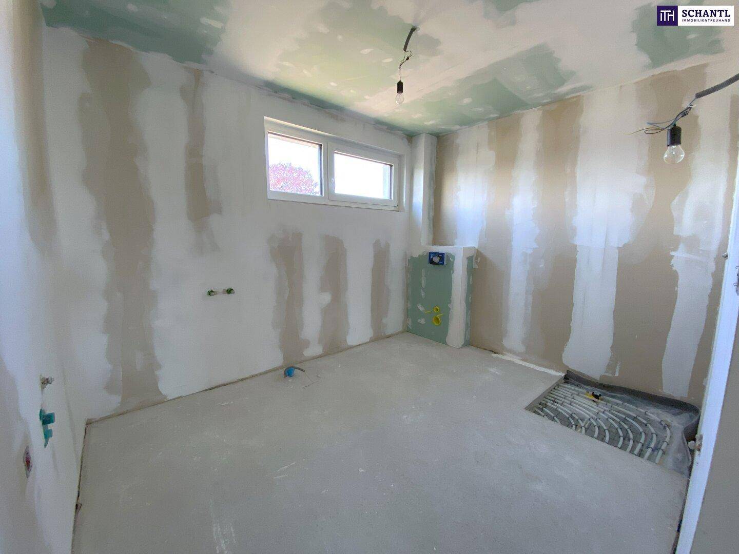 Unfertiges Badezimmer mit vorbereiteten Anschlüssen für Sanitäranlagen und Fenster.
