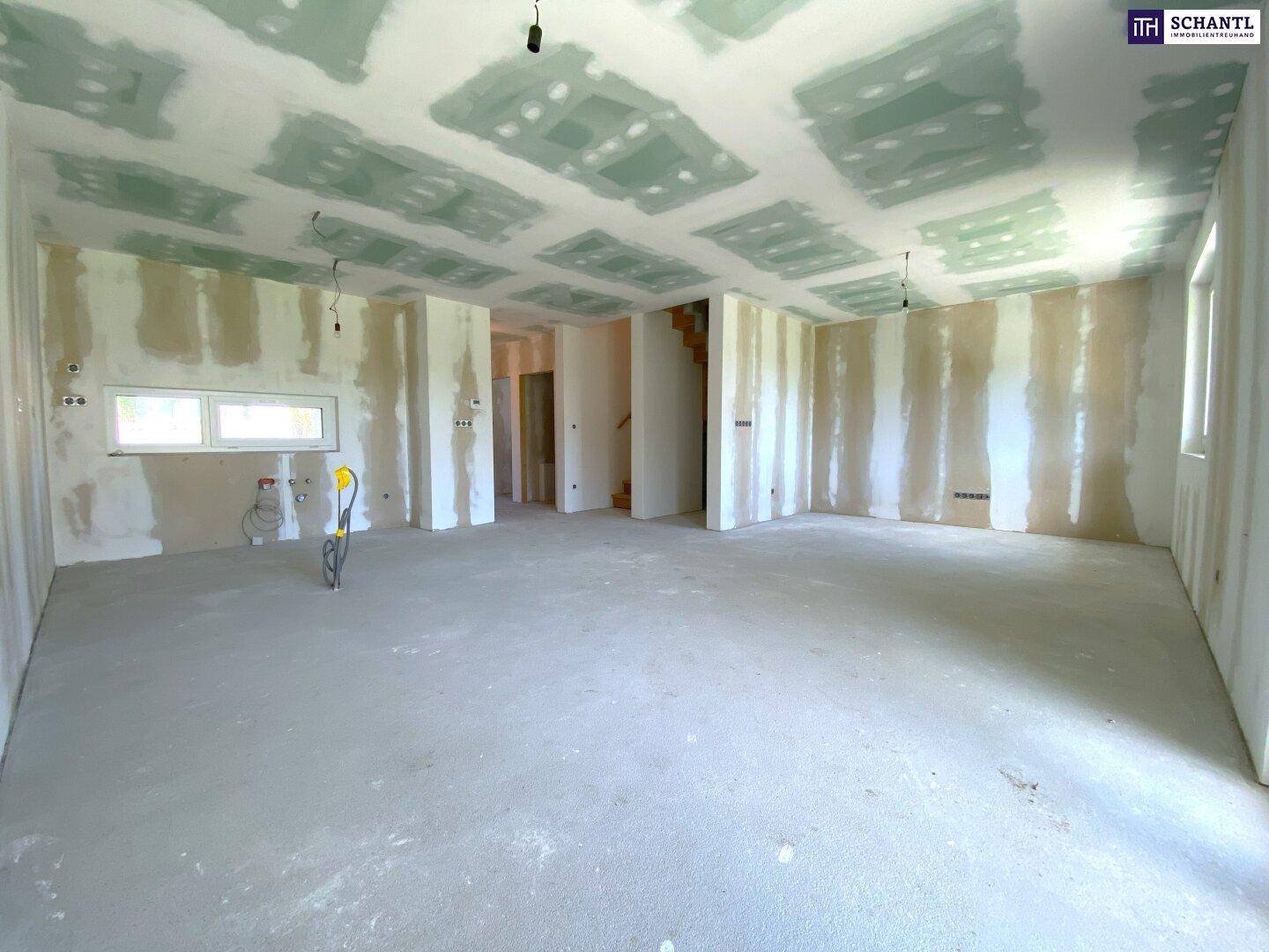 Geräumiger, unfertiger Wohnbereich mit Betonboden und vorbereiteten Wänden für den Ausbau.
