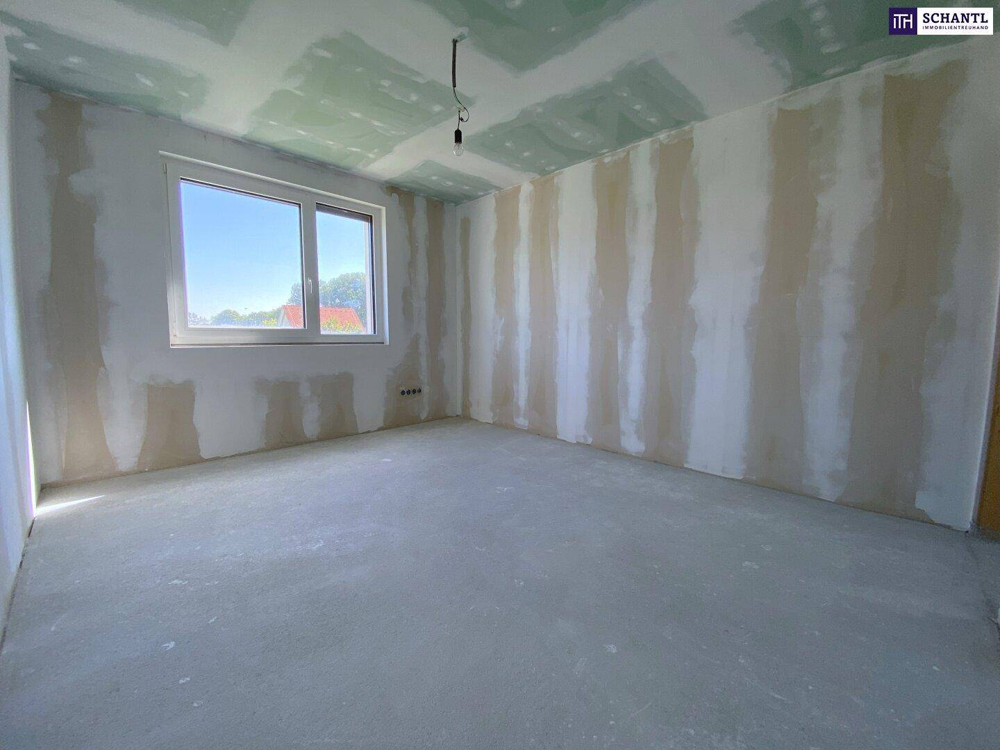Unfertiges Zimmer mit Betonboden, Trockenbauwänden und Fenster, bereit für den Ausbau.