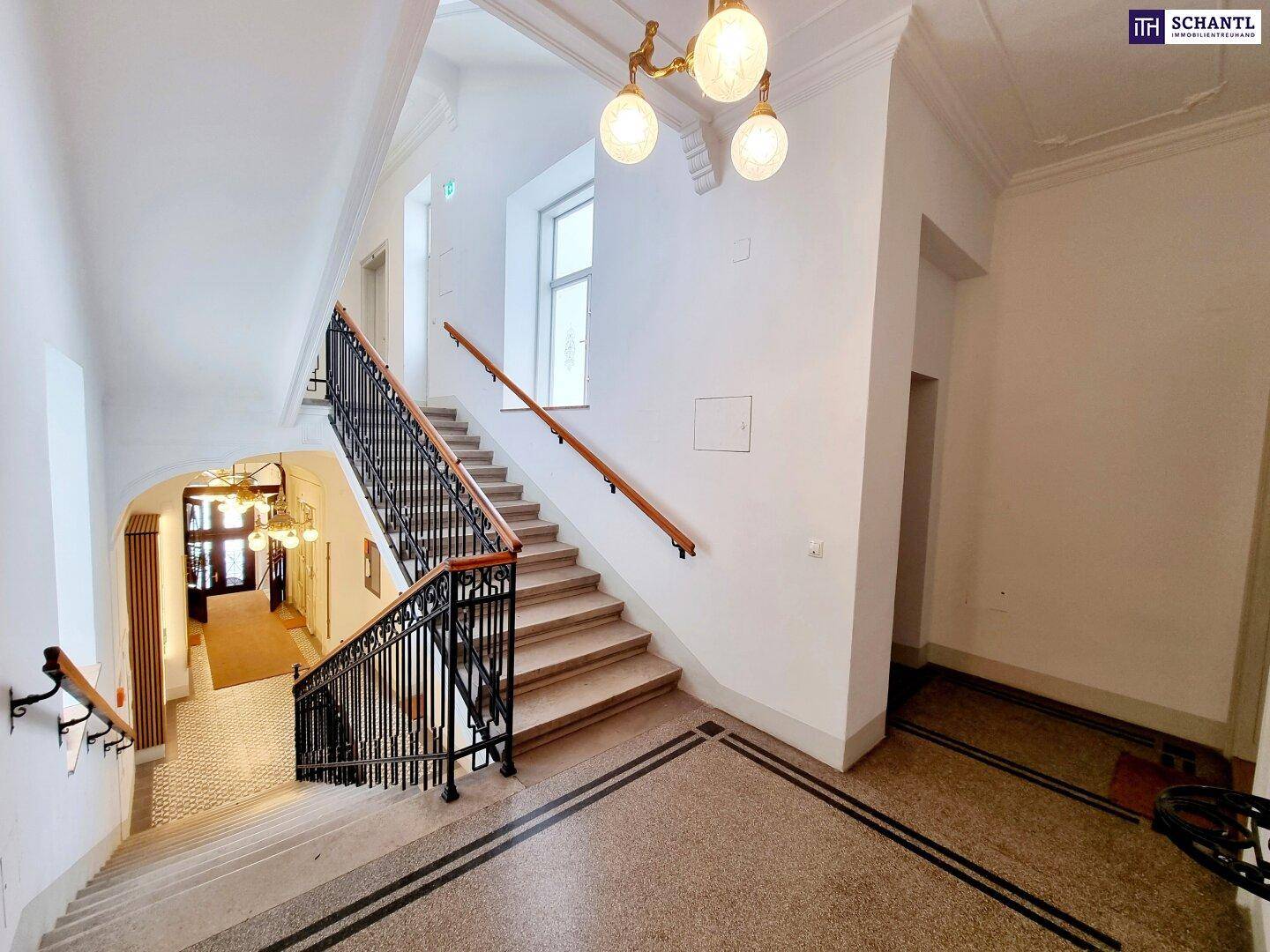 Großzügiges Treppenhaus mit breiten Stufen, natürlichem Lichteinfall und klassischer Beleuchtung.