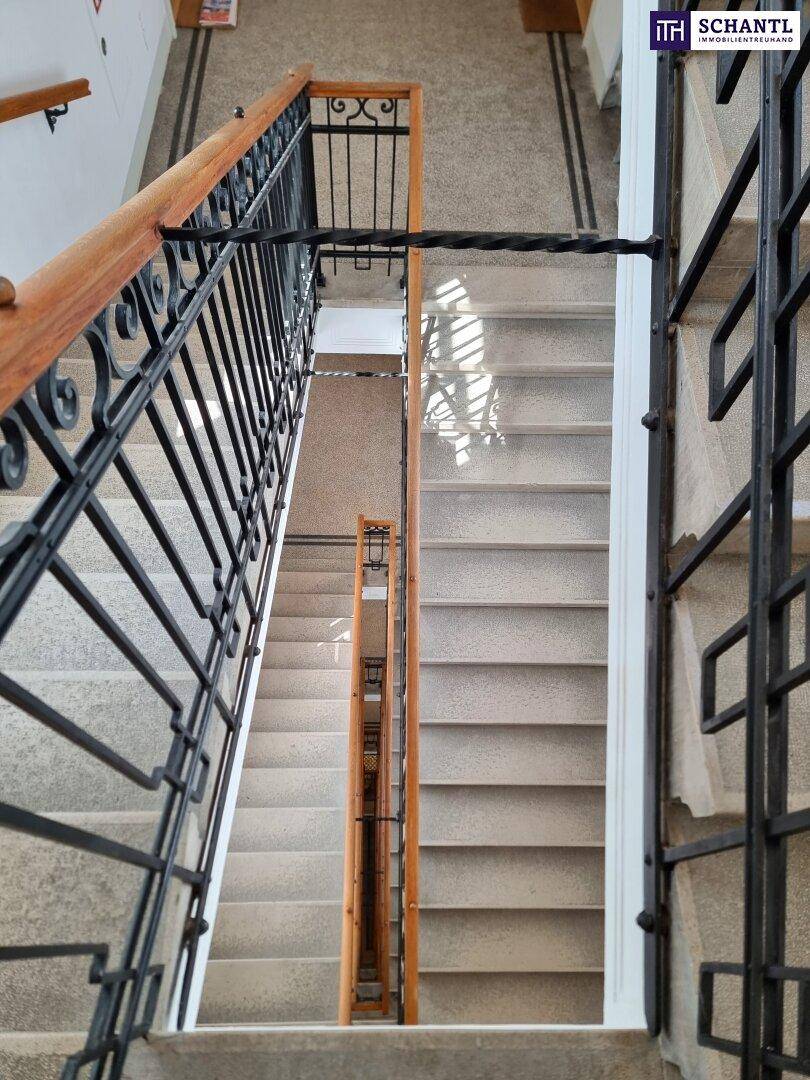 Blick von oben auf das Treppenhaus mit kunstvollem schmiedeeisernem Geländer und Holzhandlauf.