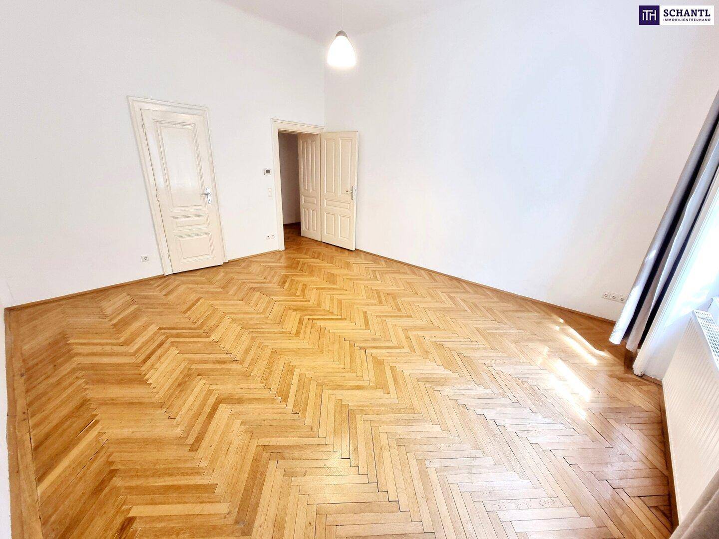 Helles Zimmer mit Fischgrätparkettboden, weißen Wänden und zwei klassischen Holztüren.