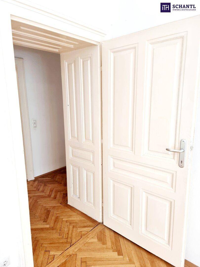 Klassische weiße Doppeltür mit Fischgrätparkettboden, die den Zugang zu einem Raum öffnet.