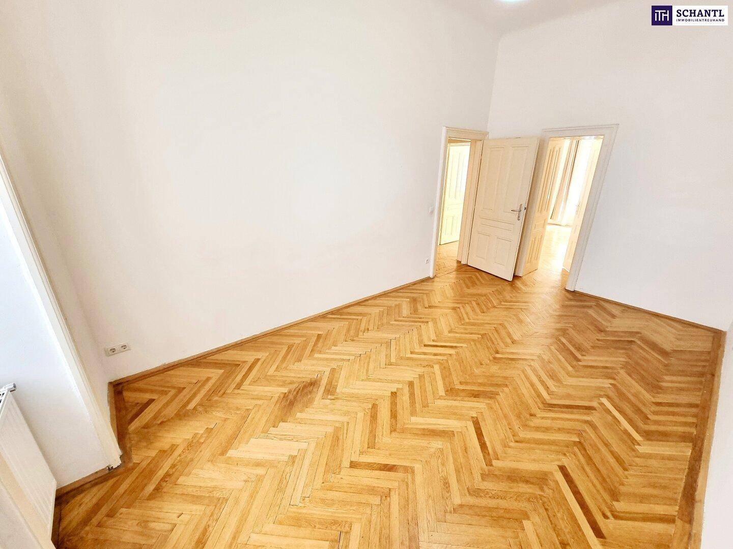 Helles Zimmer mit Fischgrätparkettboden, weißen Wänden und offenen Durchgängen zu anderen Räumen.