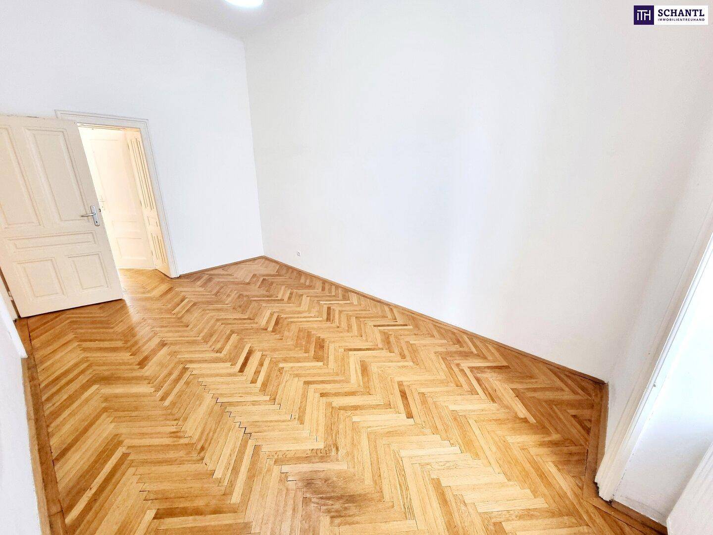 Geräumiges Zimmer mit Fischgrätparkett, hellen Wänden und einer klassischen Holztür.