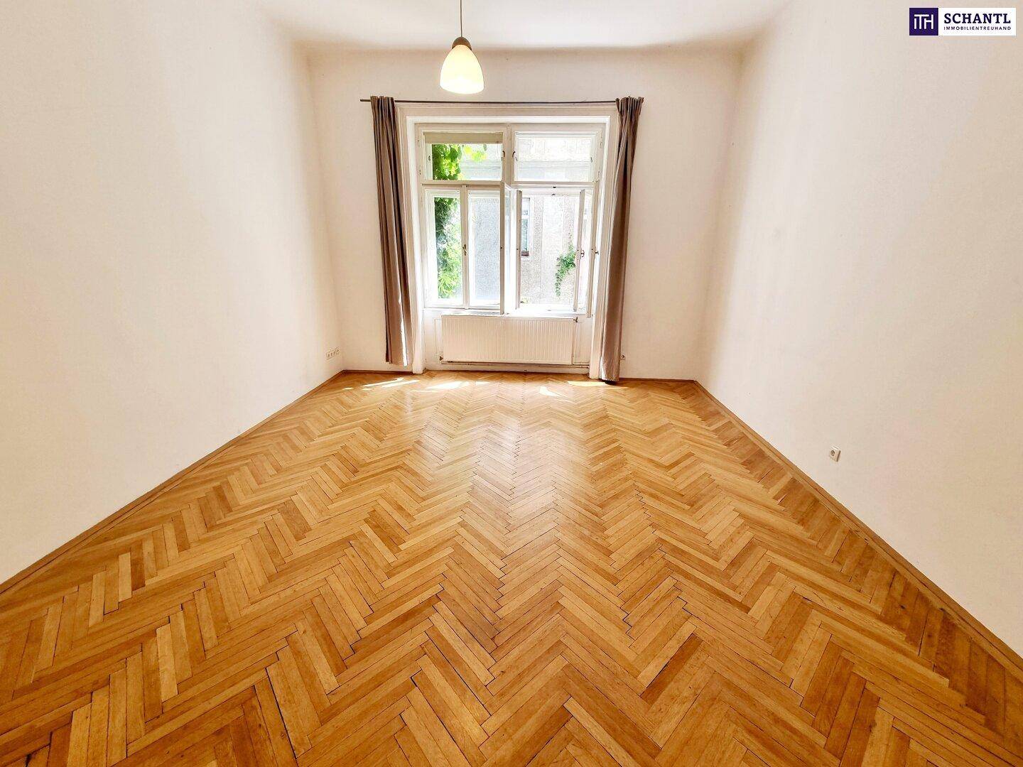 Helles und geräumiges Zimmer mit Fischgrätparkettboden und einem großen Fenster mit Blick ins Grüne.