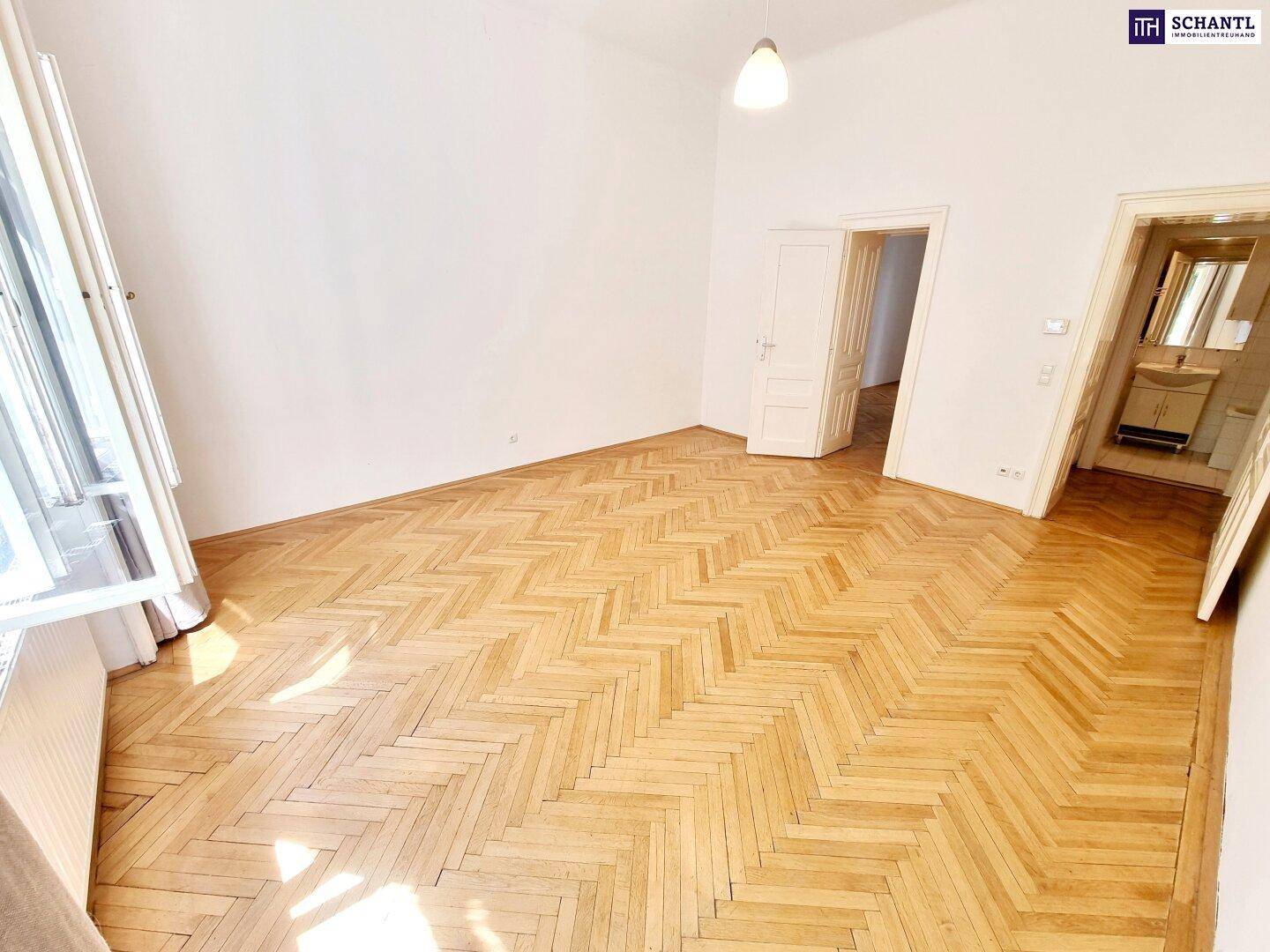 Geräumiges Zimmer mit Fischgrätparkett, hellen Wänden und Zugang zu weiteren Räumen, inklusive Bad.