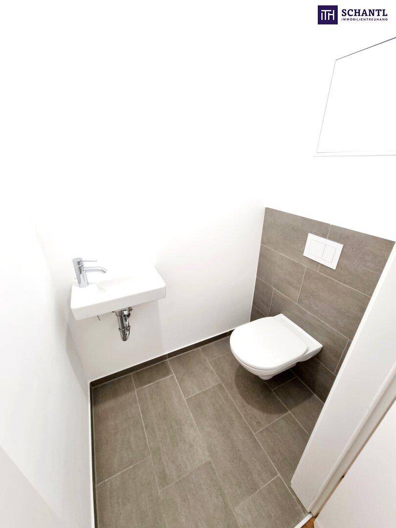 Modernes Gäste-WC mit Wand-WC, kleinem Waschbecken und grauen Fliesen.